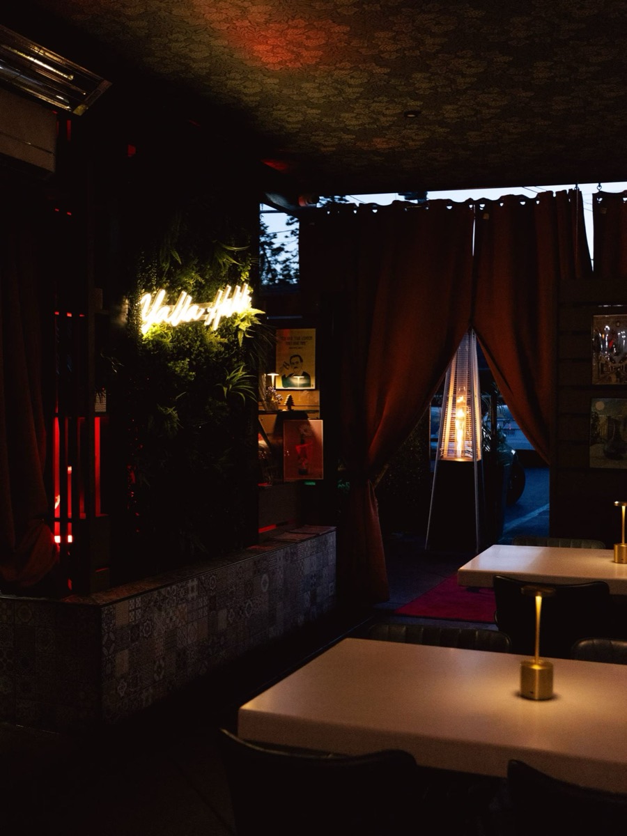 Bei's lounge at dusk, a neon sign glowing over greenery and gold table lamps